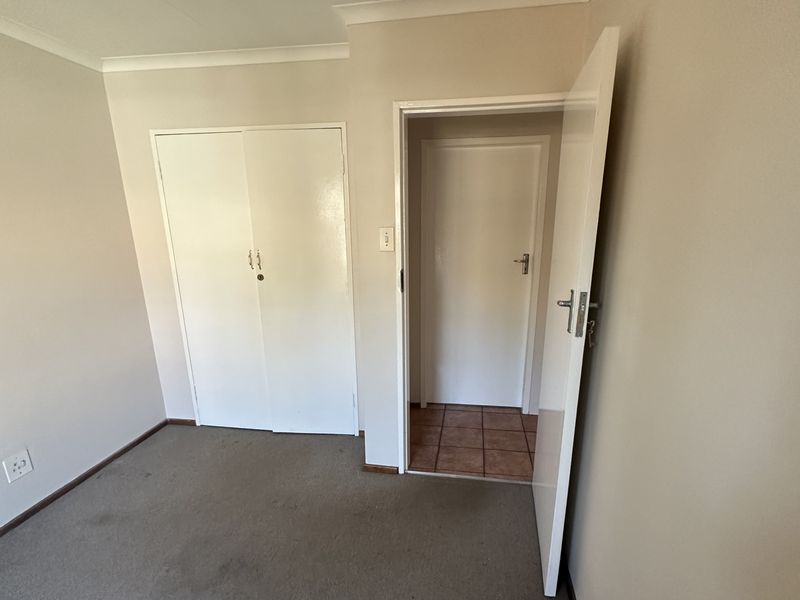 An empty bedroom featuring built-in cupboards, carpeted flooring, and a doorway leading to an adjacent tiled space.