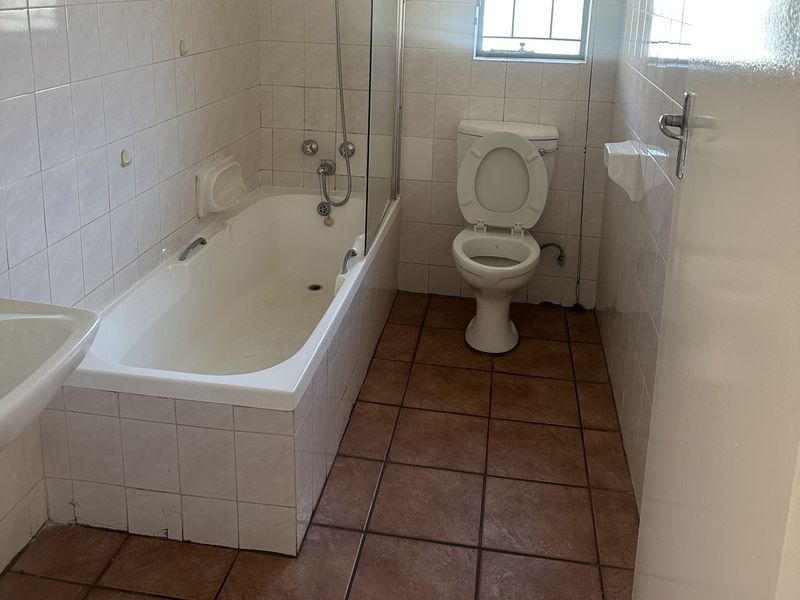 A functional bathroom featuring a bathtub with a glass screen, a toilet, and tiled finishes throughout, offering potential for modernization.