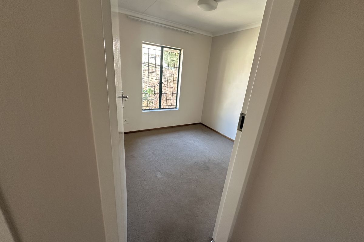 A vacant bedroom featuring neutral walls, carpeted flooring, and a window fitted with security burglar bars.