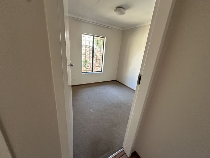 A vacant bedroom featuring neutral walls, carpeted flooring, and a window fitted with security burglar bars.