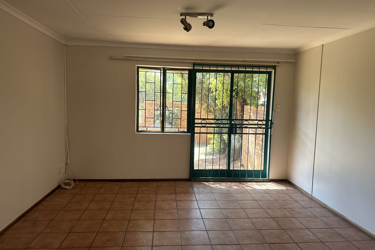 An empty living room featuring ceramic floor tiles, a sliding door with a security gate, and window security bars, offering direct access to the garden.