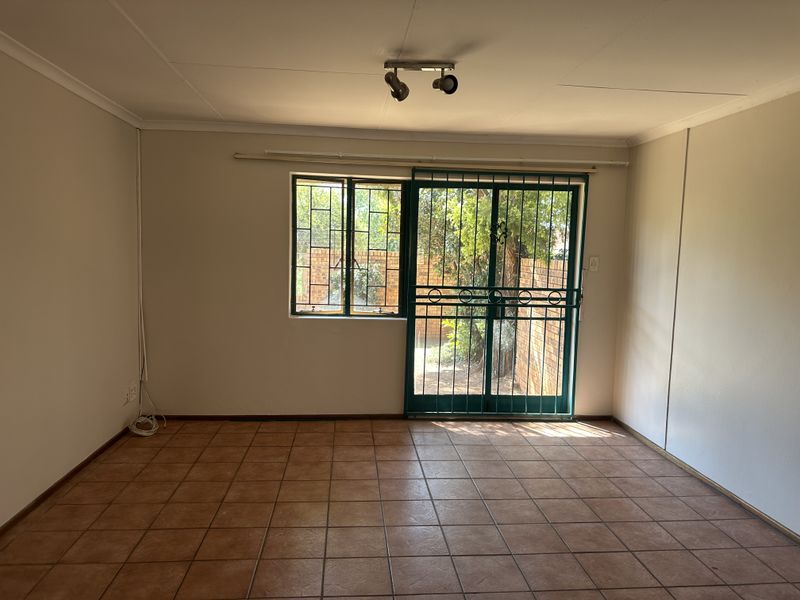 An empty living room featuring ceramic floor tiles, a sliding door with a security gate, and window security bars, offering direct access to the garden.