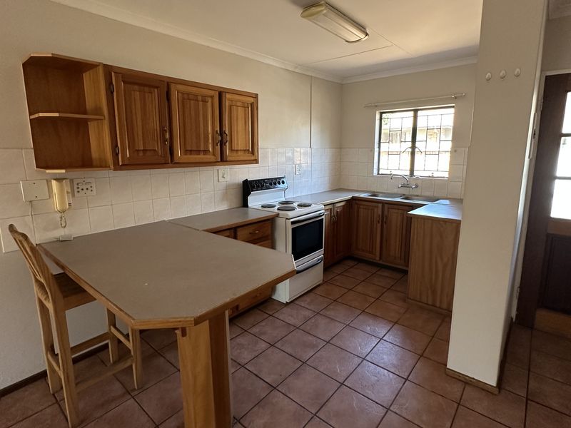 A functional kitchen featuring wooden cabinetry, tiled flooring, a breakfast counter, and a freestanding stove, offering a classic layout with potential for modernization.