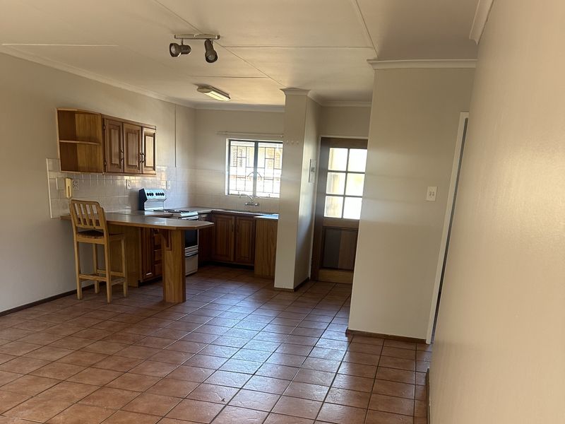 Open-plan kitchen area featuring wooden cabinetry, tiled flooring, and a built-in stove, providing a functional space with direct access to the exterior.