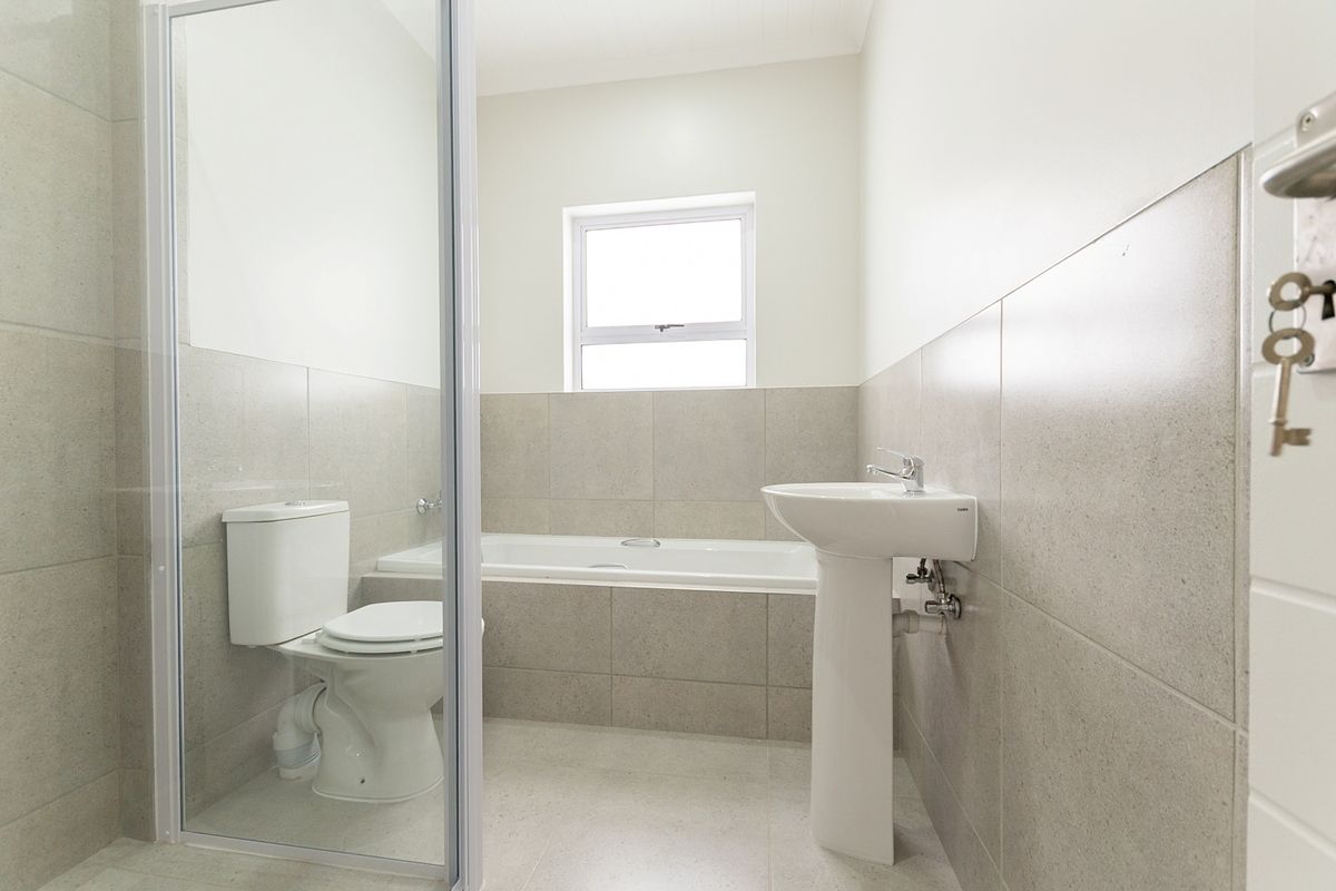 A clean, modern bathroom featuring a pedestal basin, a built-in bathtub, and a separate shower enclosure with neutral wall and floor tiling.