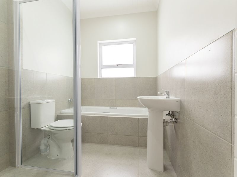 A clean, modern bathroom featuring a pedestal basin, a built-in bathtub, and a separate shower enclosure with neutral wall and floor tiling.