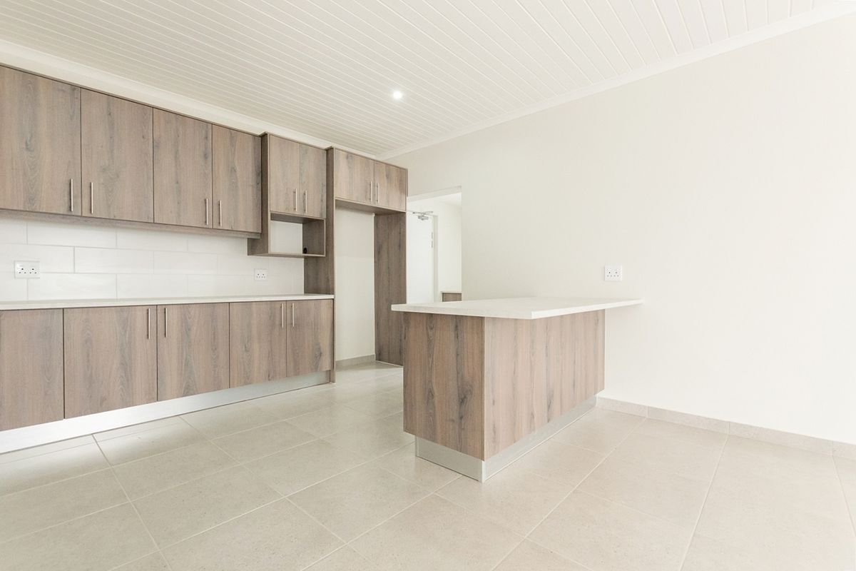 Modern kitchen featuring wood-look cabinetry, a central island, subway tile backsplash, and neutral tiled flooring in a clean, empty space.