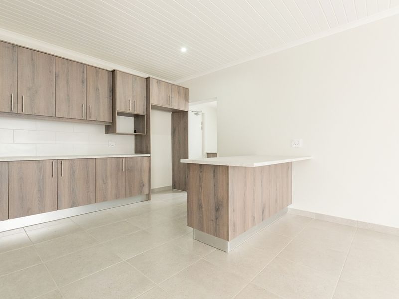 Modern kitchen featuring wood-look cabinetry, a central island, subway tile backsplash, and neutral tiled flooring in a clean, empty space.