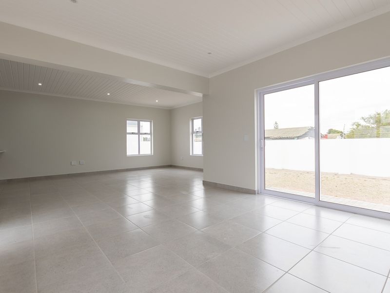 Spacious open-plan living area featuring neutral tiled flooring, recessed lighting, and large sliding glass doors providing access to the rear exterior.