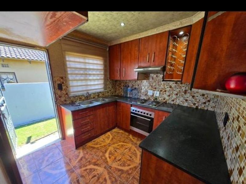 A functional kitchen featuring wood-finish cabinetry, granite countertops, a mosaic tile backsplash, and integrated appliances, with direct access to the exterior.