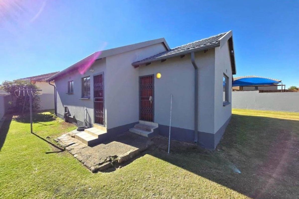 Rear view of the house featuring a concrete pathway, security gates, and a well-maintained lawn area.
