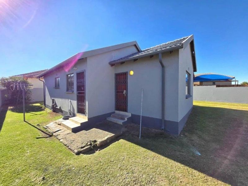 Rear view of the house featuring a concrete pathway, security gates, and a well-maintained lawn area.