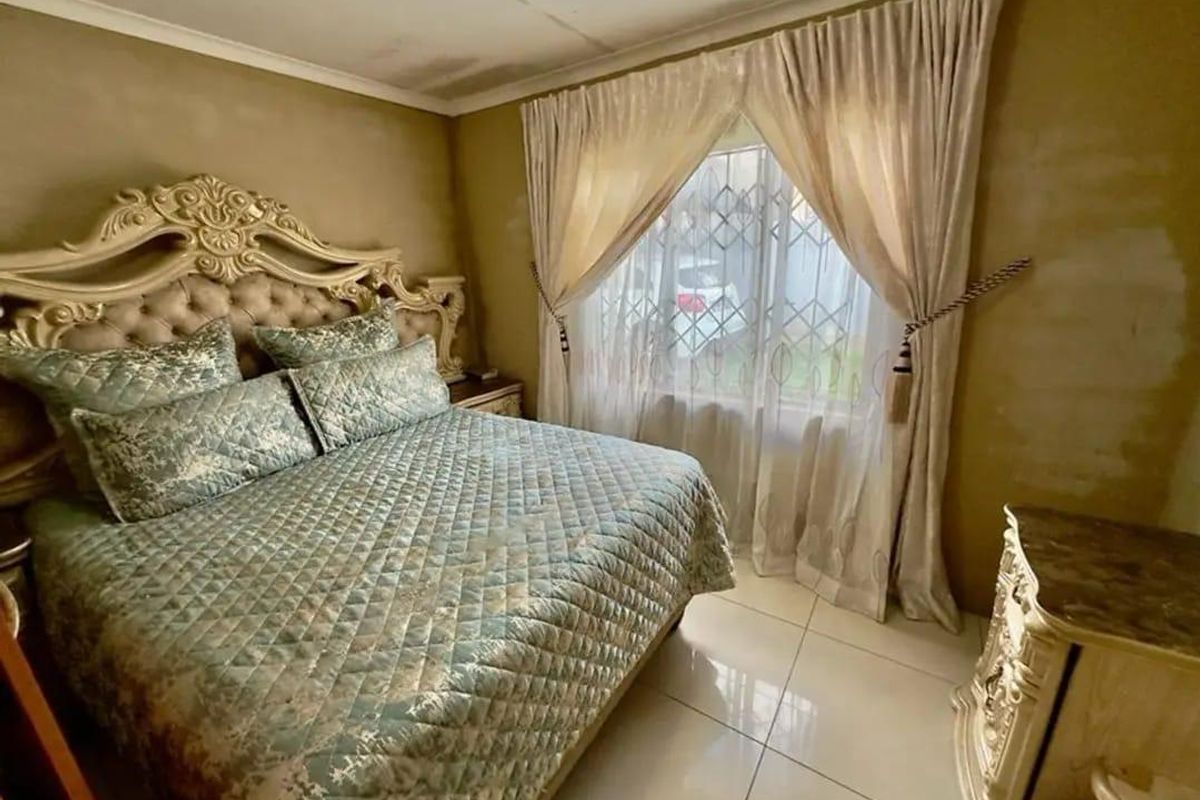 A bedroom featuring tiled flooring and security burglar bars on the window, with walls requiring cosmetic attention and repainting.