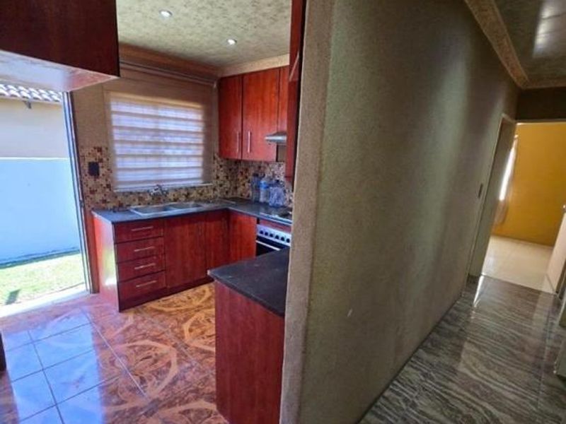 A functional kitchen featuring built-in cabinetry, laminate countertops, and tiled flooring, with direct access to the outdoor area.
