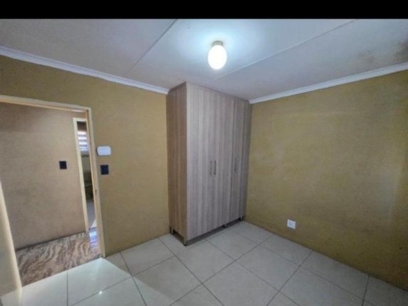 An empty bedroom featuring tiled flooring and a built-in wardrobe, requiring cosmetic updates to the walls and ceiling.