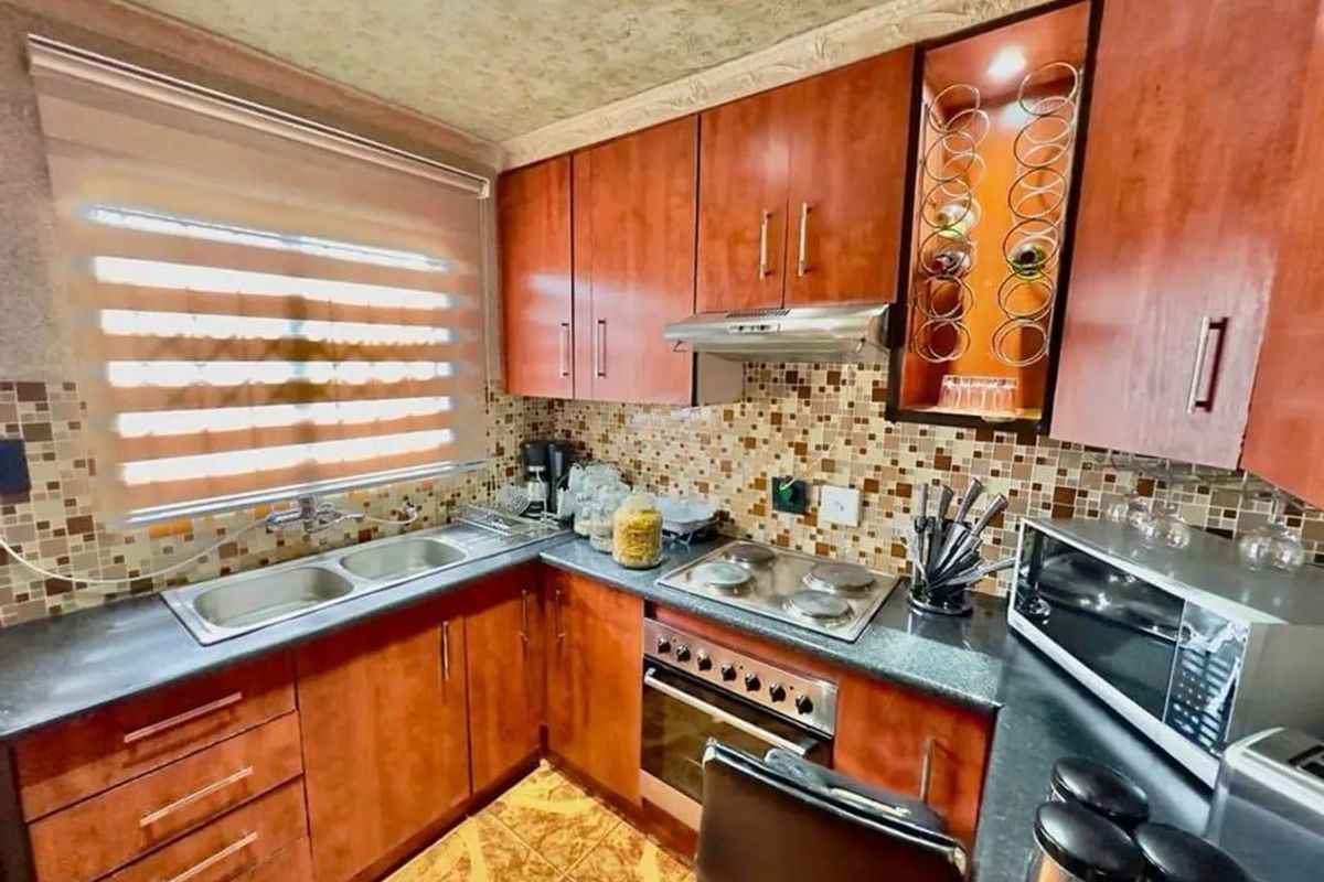A functional kitchen featuring wood-finish cabinetry, mosaic tile backsplash, integrated electric hob and oven, and a double sink with a window view.