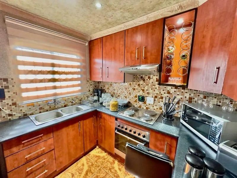A functional kitchen featuring wood-finish cabinetry, mosaic tile backsplash, integrated electric hob and oven, and a double sink with a window view.