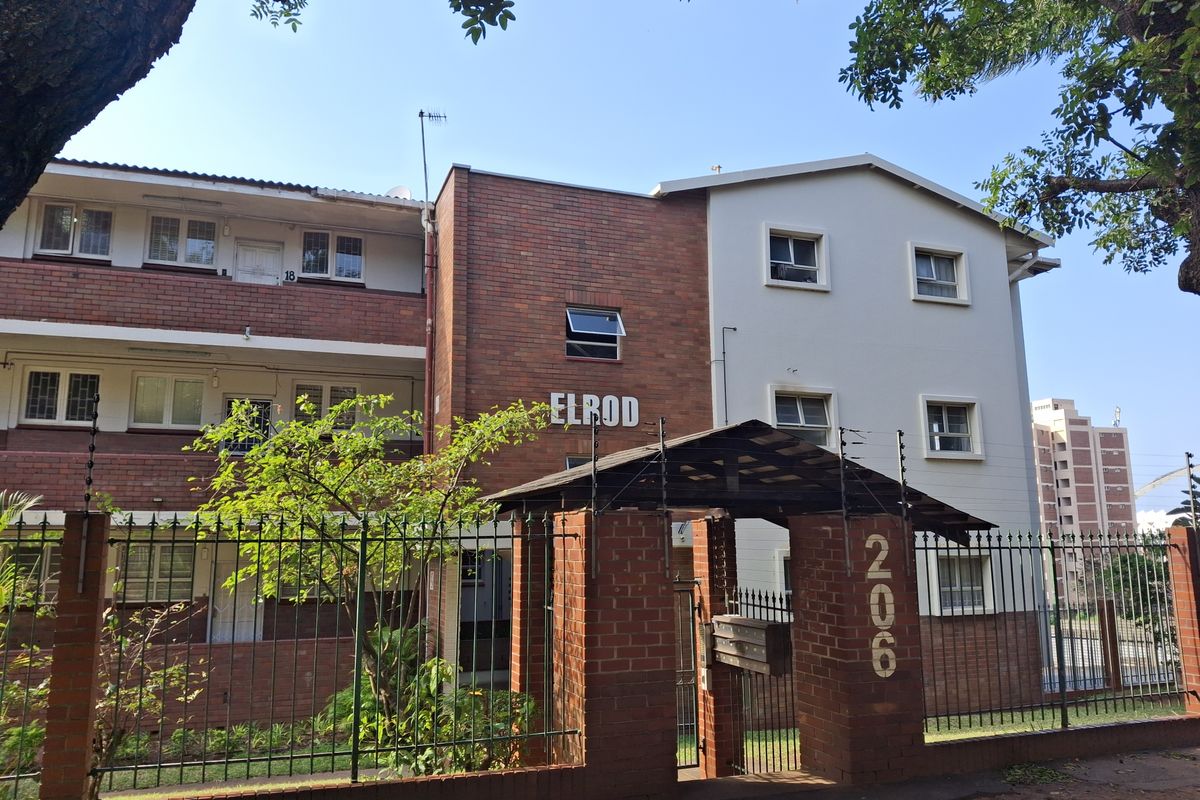 Front elevation of the Elrod apartment complex, featuring a brick and rendered facade, secure perimeter fencing, and gated entrance.