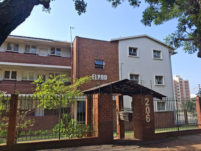 Front elevation of the Elrod apartment complex, featuring a brick and rendered facade, secure perimeter fencing, and gated entrance.