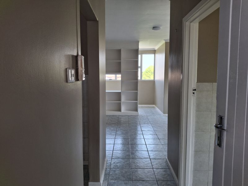 A bright hallway with tiled flooring leading into an open living area featuring built-in shelving and natural light.