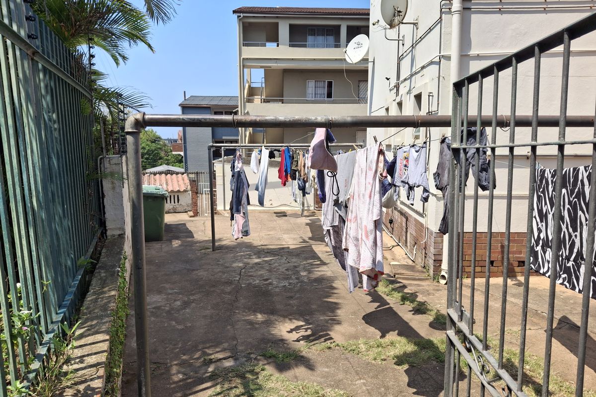 A rear exterior utility area featuring concrete paving, metal security fencing, and external building infrastructure.