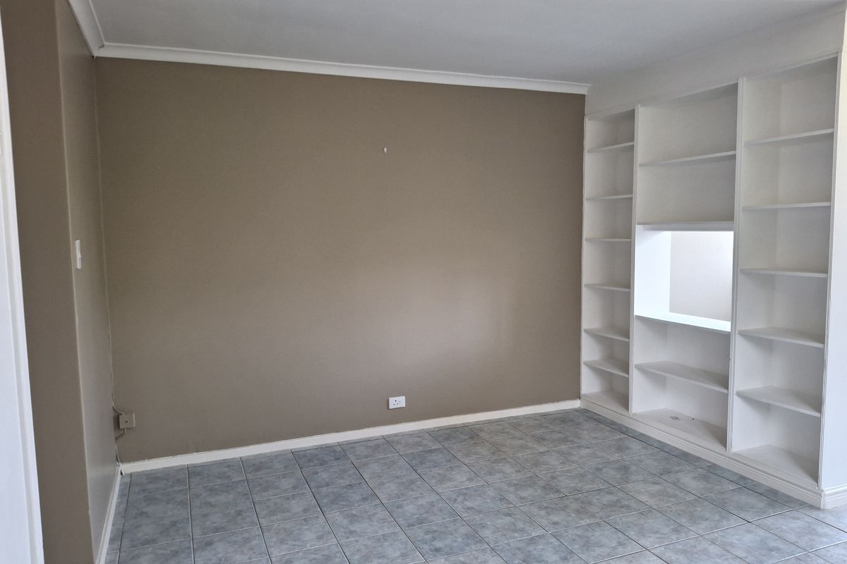 An empty living area featuring neutral wall tones, tiled flooring, and integrated white built-in shelving units.
