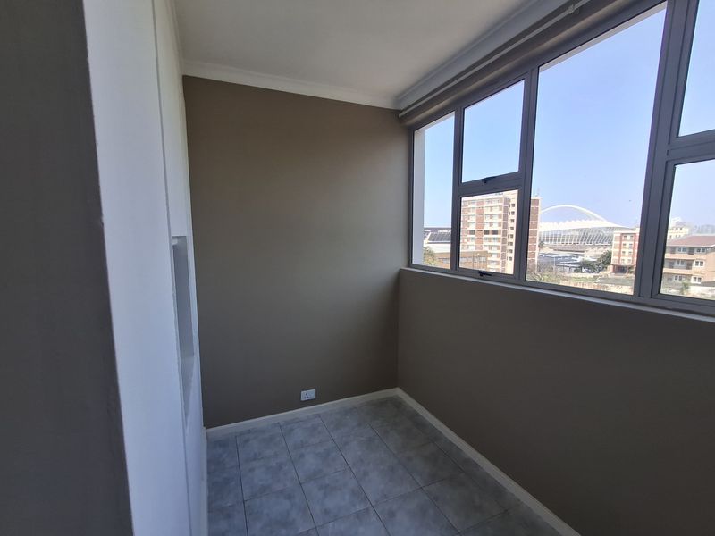 An enclosed balcony featuring tiled flooring and large windows offering an urban view, providing a versatile space for a sunroom or study area.