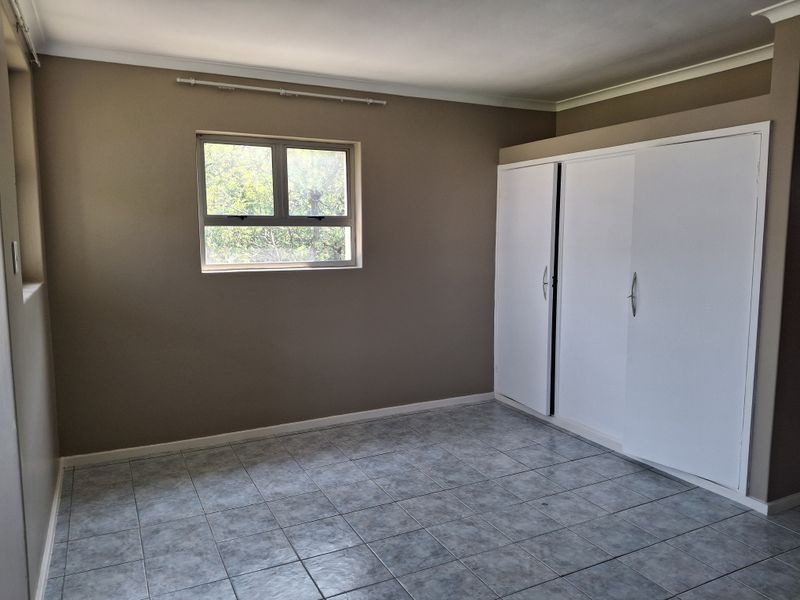 A clean, empty bedroom featuring neutral wall paint, tiled flooring, and built-in white cupboards with ample storage space.