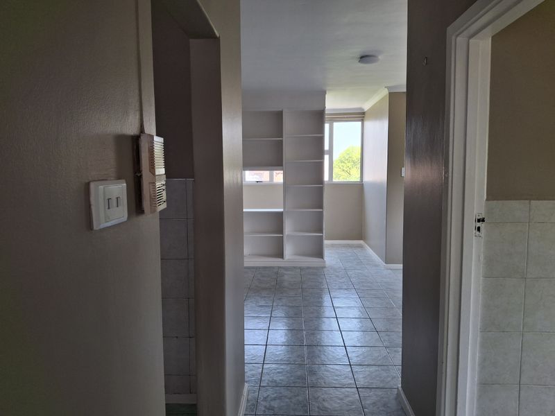 A view through a hallway into an open living area featuring tiled flooring and a built-in white shelving unit.