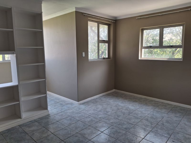 An empty bedroom featuring tiled flooring, built-in shelving, and aluminium window frames, offering a neutral canvas for personalization.