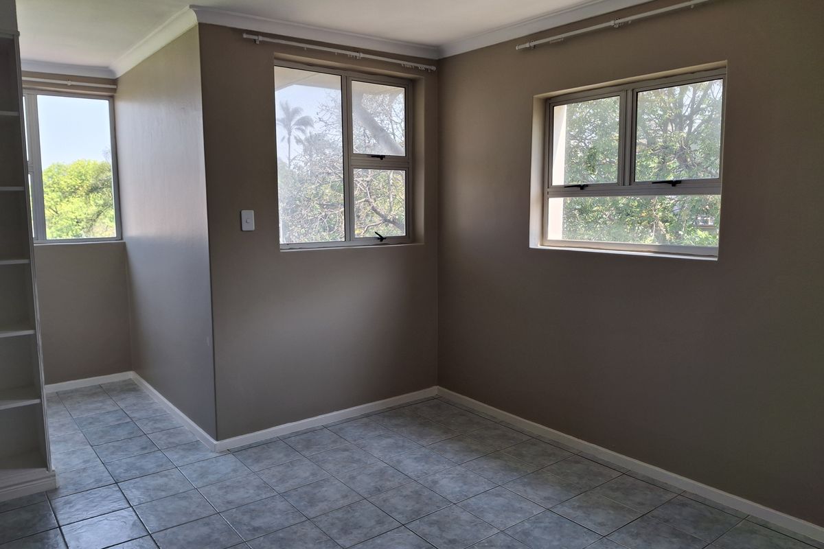 A bright, empty bedroom featuring neutral wall paint, tiled flooring, and built-in shelving, offering a clean canvas for personalization.