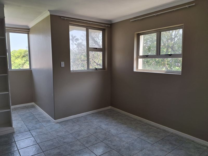 A bright, empty bedroom featuring neutral wall paint, tiled flooring, and built-in shelving, offering a clean canvas for personalization.