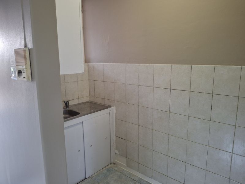 A compact scullery or utility area featuring a stainless steel sink, built-in cabinetry, and tiled splashback, requiring cosmetic updates.