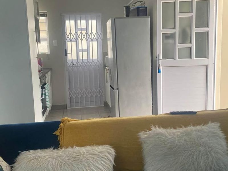 Open plan living area featuring tiled flooring, panelled ceilings, and direct access to a kitchen space with built-in cabinetry and a security gate.