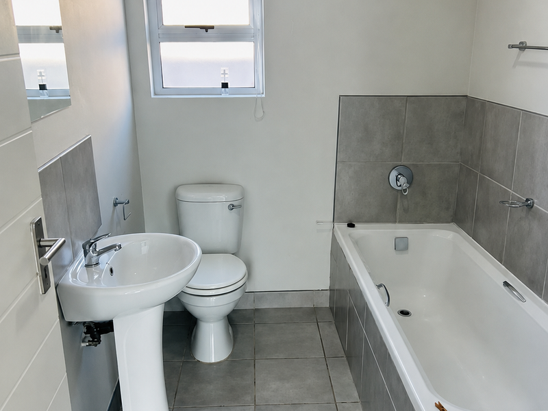 A clean, functional bathroom featuring a pedestal basin, toilet, and bathtub with neutral grey floor and wall tiling.
