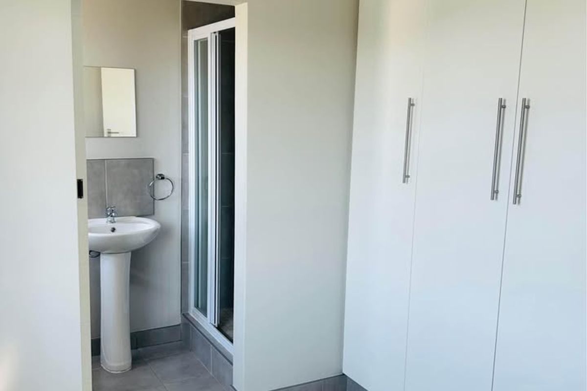 A clean, empty bedroom featuring built-in cupboards and an en-suite bathroom with a pedestal basin and shower enclosure.