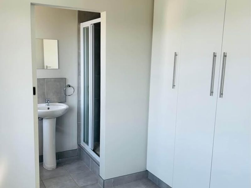 A clean, empty bedroom featuring built-in cupboards and an en-suite bathroom with a pedestal basin and shower enclosure.