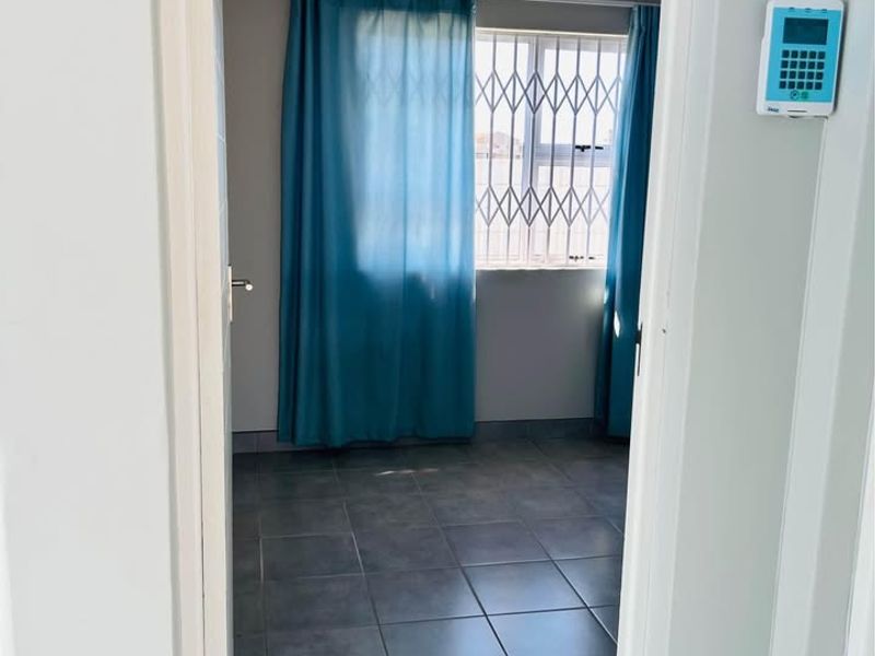 A clean, empty bedroom featuring neutral grey tiled flooring, cornicing, and a security gate on the window, with an alarm system keypad installed.