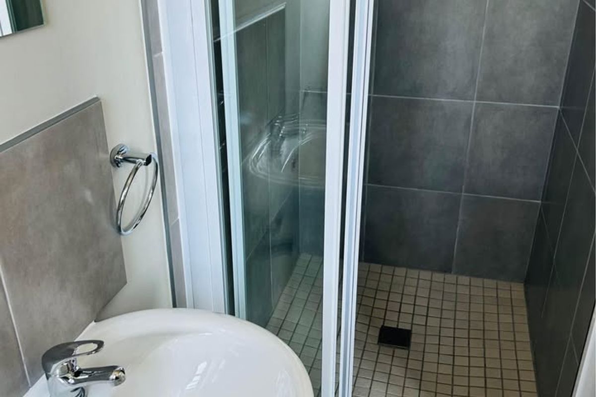A clean, modern bathroom featuring a pedestal washbasin with chrome fixtures and a separate shower enclosure with sliding glass doors and tiled finishes.