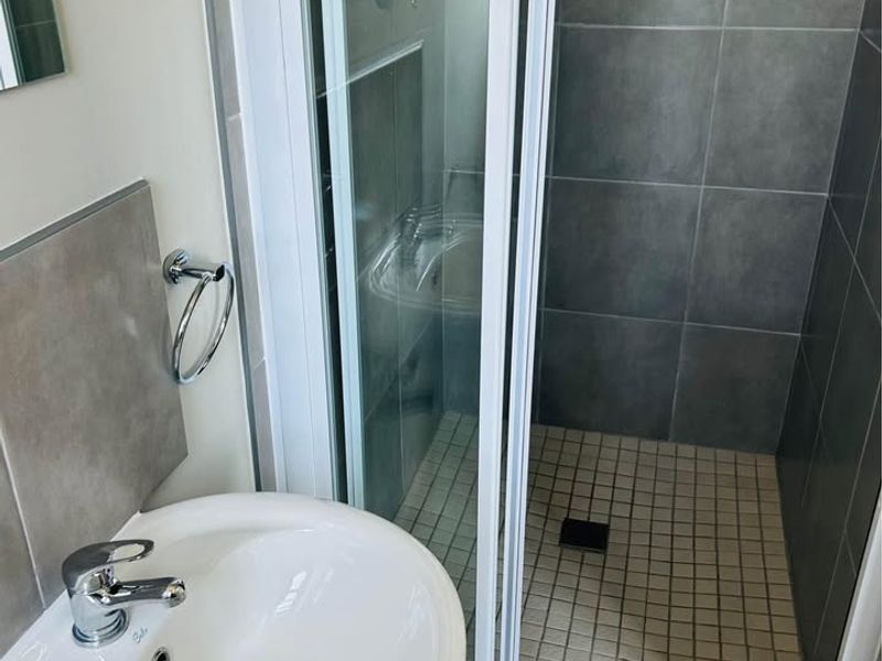 A clean, modern bathroom featuring a pedestal washbasin with chrome fixtures and a separate shower enclosure with sliding glass doors and tiled finishes.