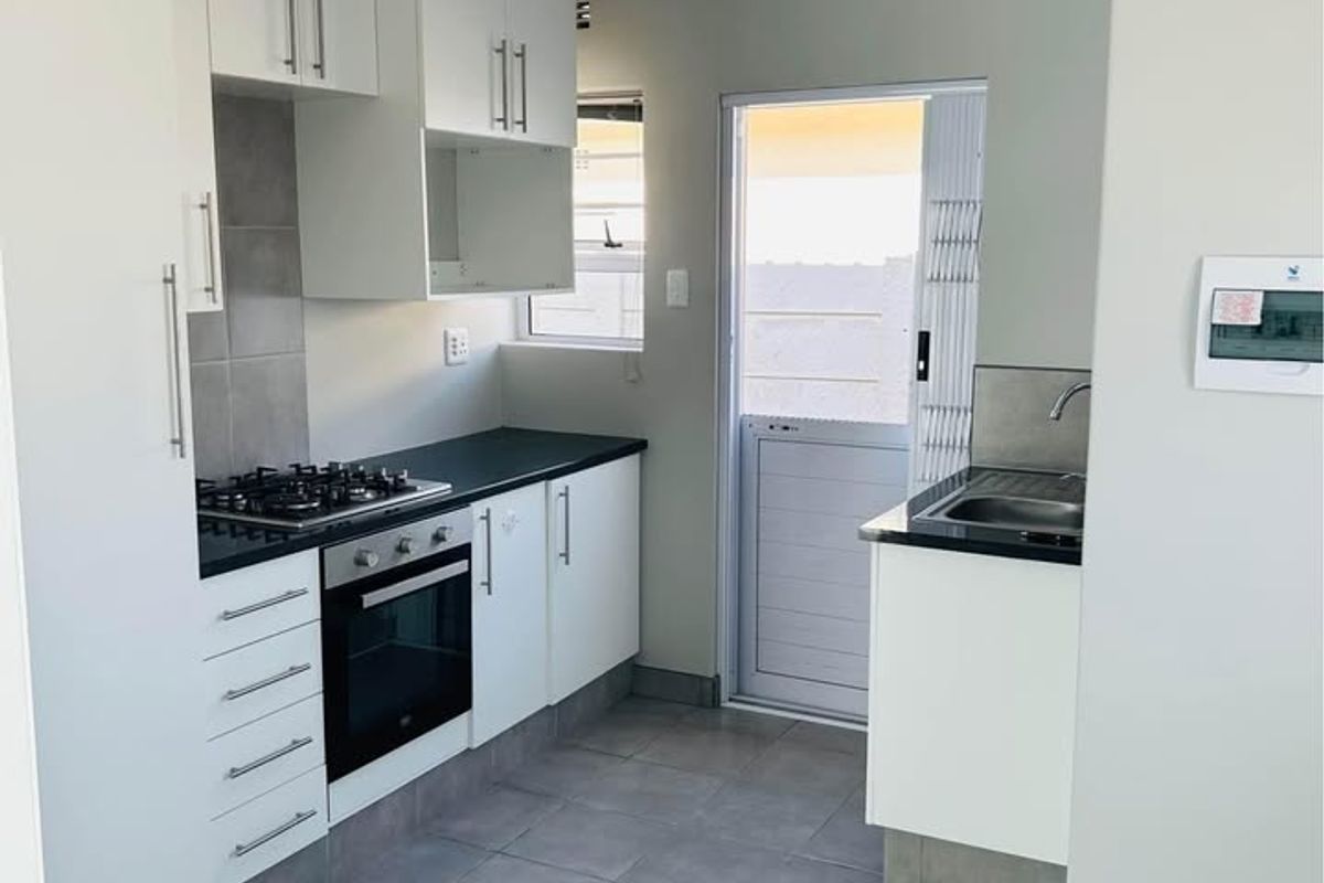 A clean, modern kitchen featuring white cabinetry, dark countertops, a gas hob, built-in oven, and direct access to an outdoor area.