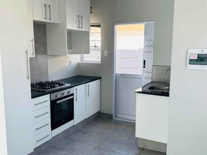 A clean, modern kitchen featuring white cabinetry, dark countertops, a gas hob, built-in oven, and direct access to an outdoor area.
