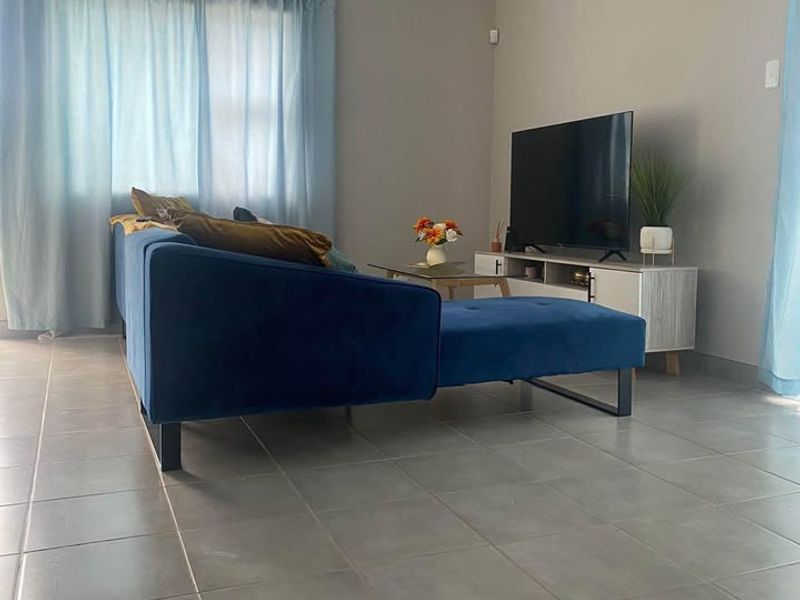 A living room featuring neutral grey tiled flooring, coved cornicing, and recessed ceiling lighting, providing a clean and functional space.