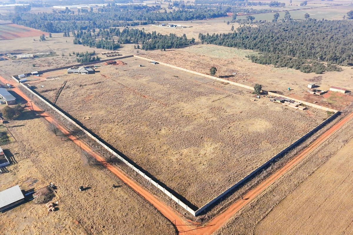 Aerial view of a large, vacant residential plot enclosed by a perimeter wall, situated in a rural landscape.