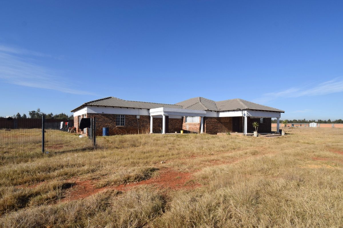 Rear view of a single-story brick residential property featuring a covered patio area, set on a large, undeveloped plot of land.
