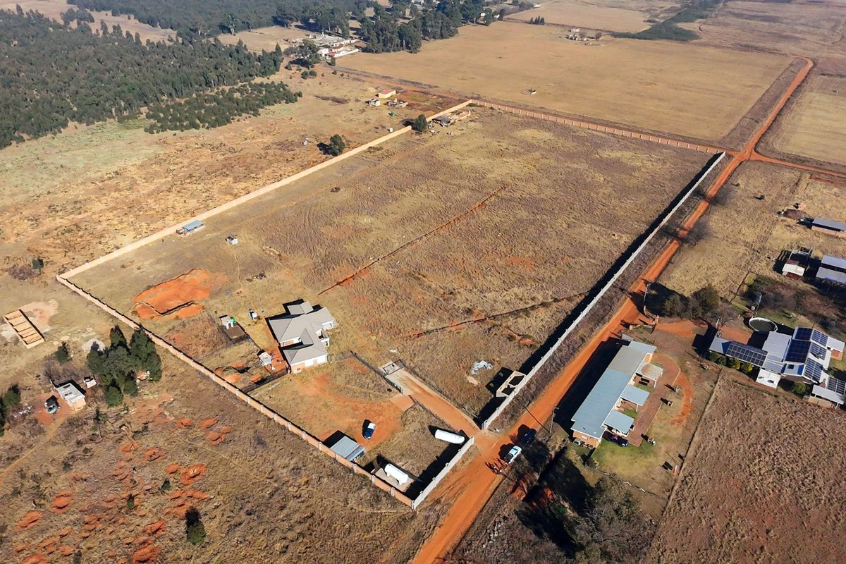 Aerial view of a large residential plot featuring a main dwelling, outbuildings, and perimeter fencing in a rural setting.
