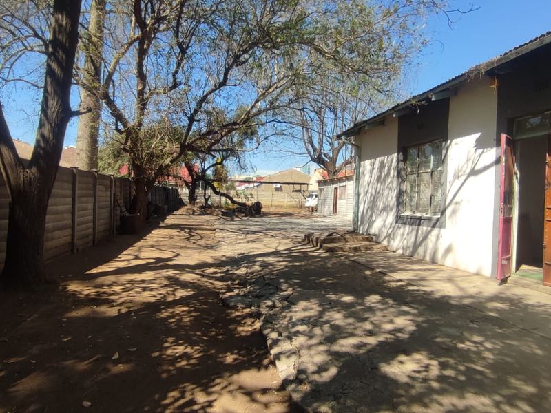 Rear exterior view of the property featuring a concrete apron, precast boundary wall, and mature trees in the backyard area.