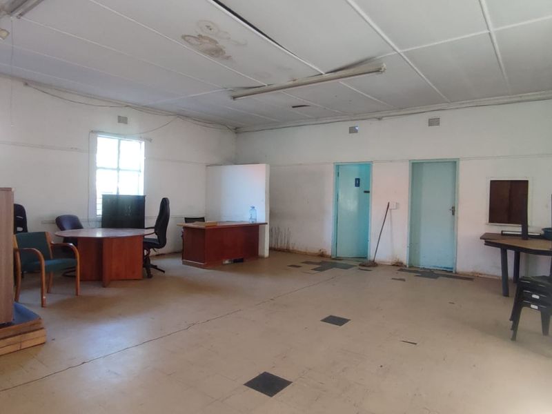 A spacious office area featuring tiled flooring and fluorescent lighting, currently in need of cosmetic refurbishment and ceiling repairs.