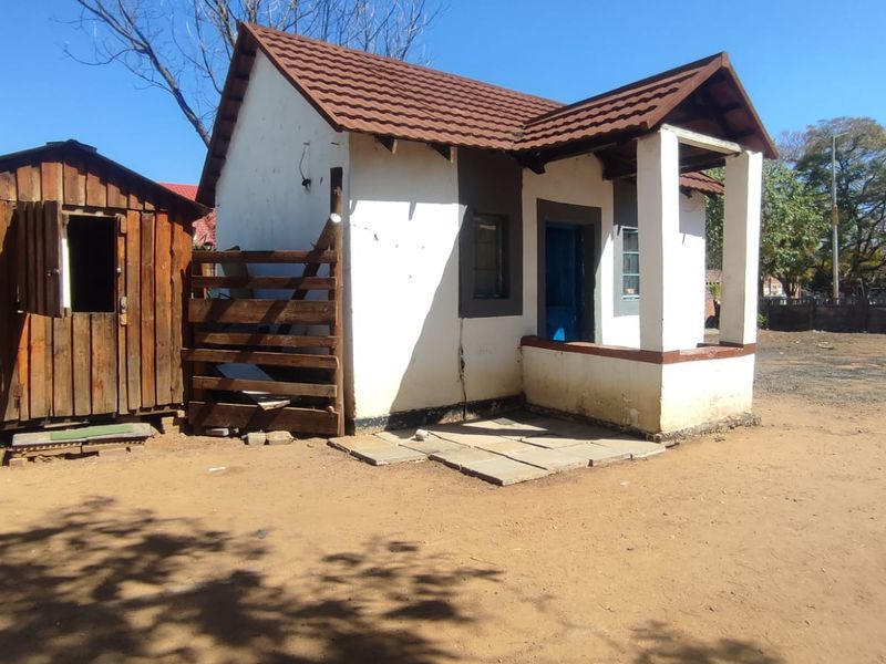 A small detached structure featuring a tiled roof and a covered porch, showing signs of significant exterior wear and structural weathering.