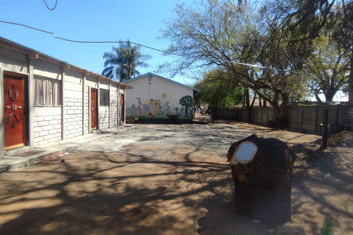 A view of the rear exterior area featuring a concrete block building with timber doors and a large unpaved yard space.